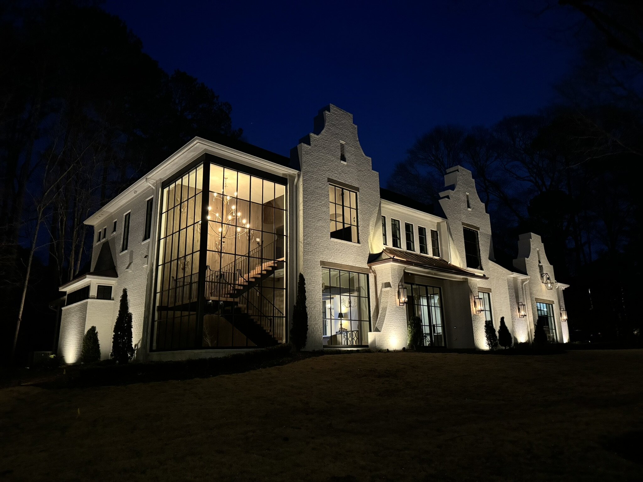 A custom Georgia stone estate illuminated at night with warm architectural uplighting against a deep navy sky.
