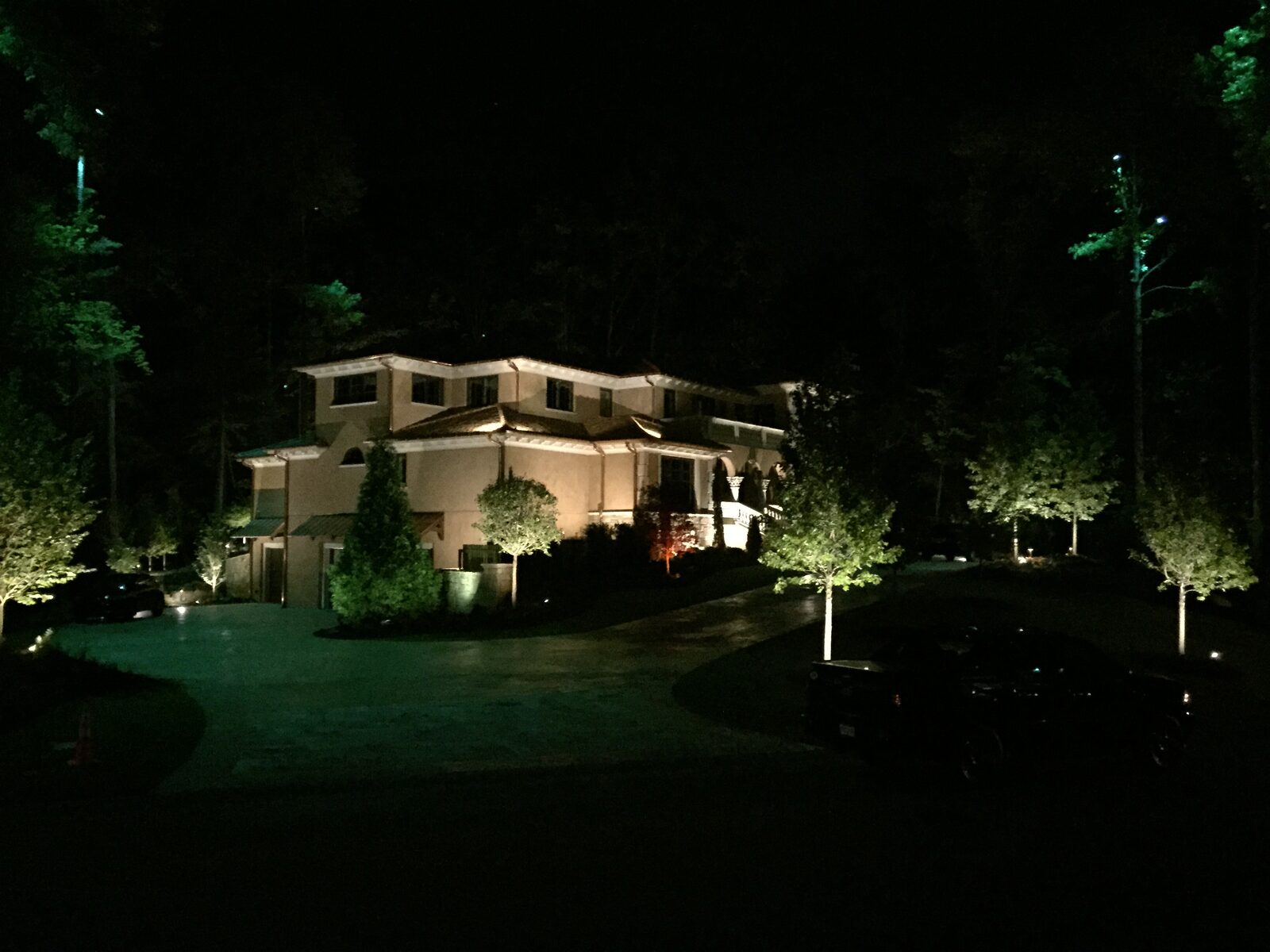 Large estate home with full-property uplighting on gables, trees, and driveway.