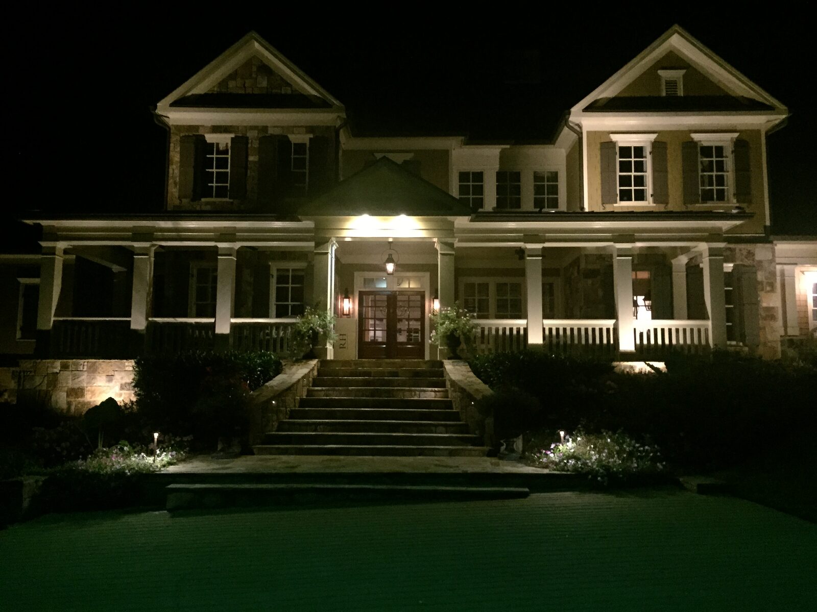Craftsman-style home with stone pillar and porch lit with warm wall-wash lighting.