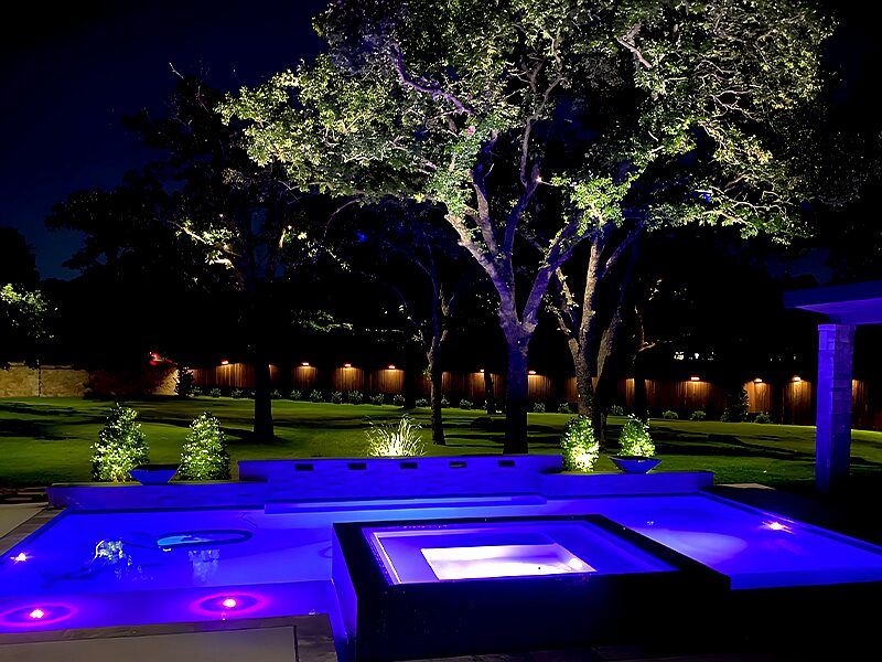Backyard pool and spa lit in blue and purple color-changing light.