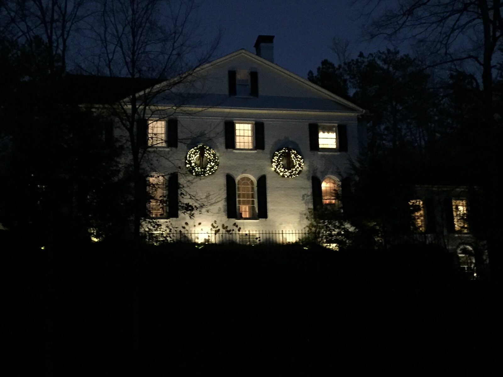 Brick colonial home with lit holiday wreaths in the upstairs windows.