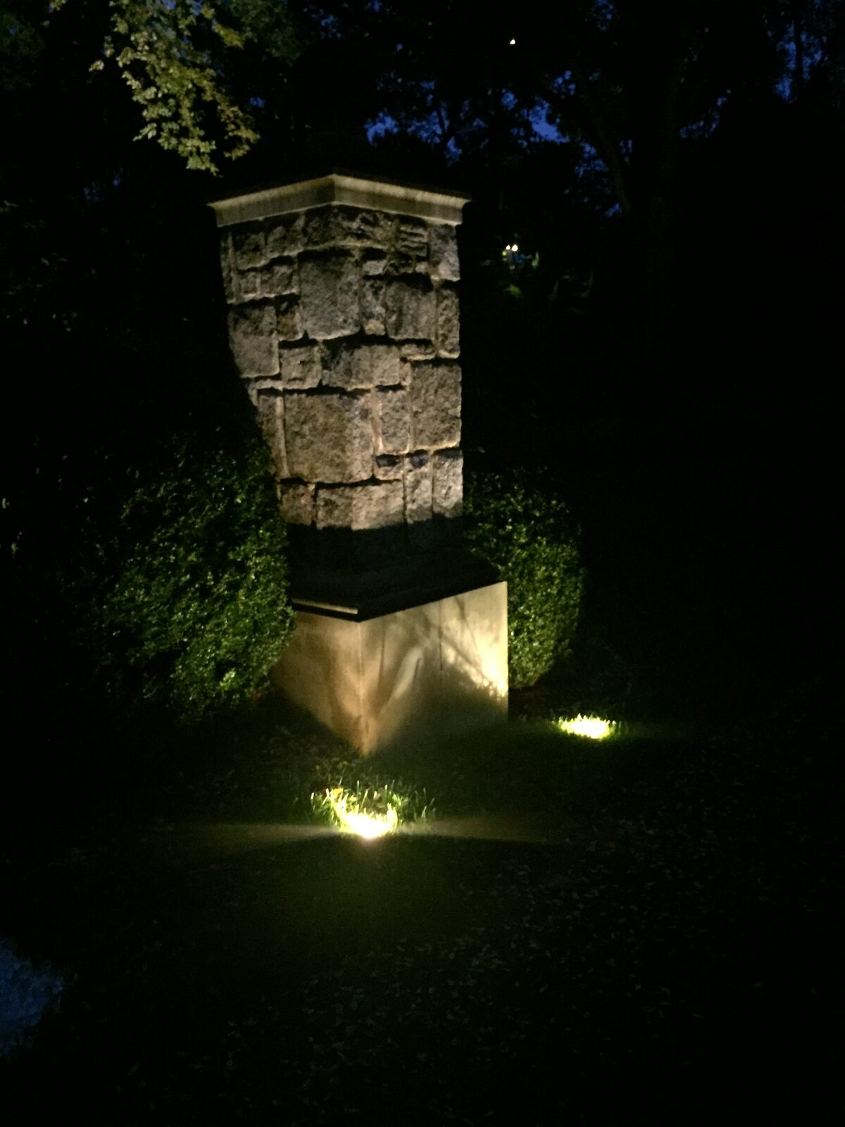 Textured stone entry monument lit from two angles at night.
